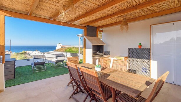 Zona de menjador a l'aire lliure amb vistes al mar, una barbacoa i un patí amb cadires i taula.