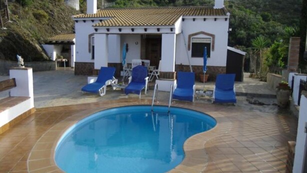 A swimming pool with blue lounge chairs and a small building with a tiled roof. - Cortijo el Maurel Cajiz by Ruralidays (Málaga)