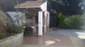 A small outdoor patio area with a table and chairs, a tiled roof structure, and a stone wall. - Cortijo el Maurel Cajiz by Ruralidays (Málaga)