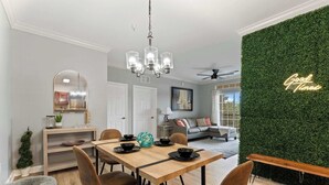 Uma sala de jantar com mesa de madeira, cadeiras e um candelabro. Uma parede verde com a inscrição 'Good Times'.