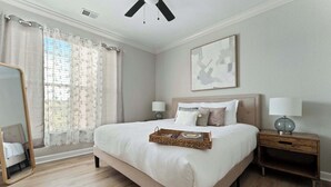 Quarto com uma cama grande, duas mesas de cabeceira com luminárias, um espelho e uma obra de arte abstrata emoldurada na parede.