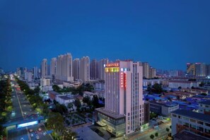 Un hotel moderno de gran altura con varias plantas, un letrero llamativo y un paisaje urbano de fondo.