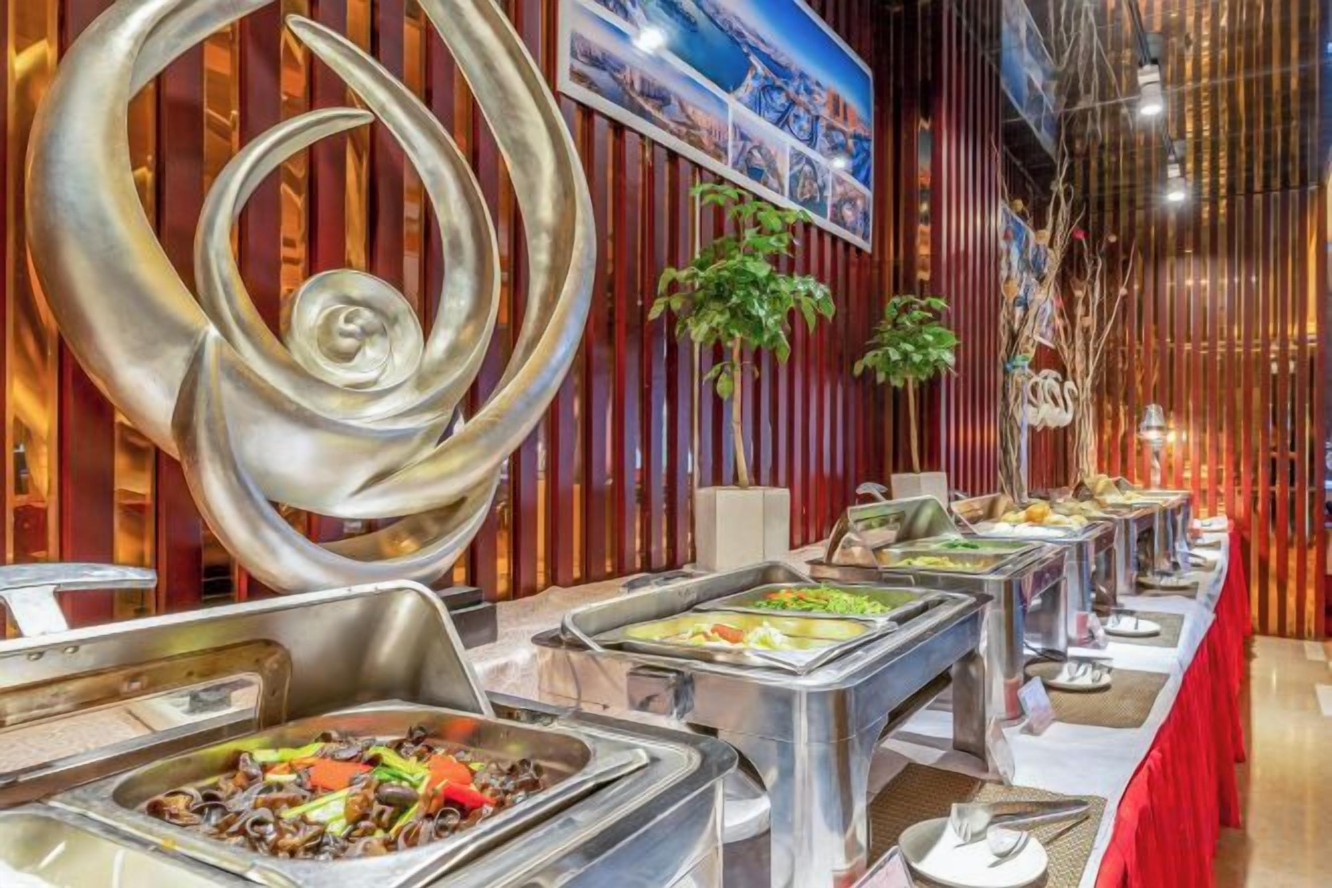 A buffet with various food options, a decorative metal sculpture, and a red tablecloth.