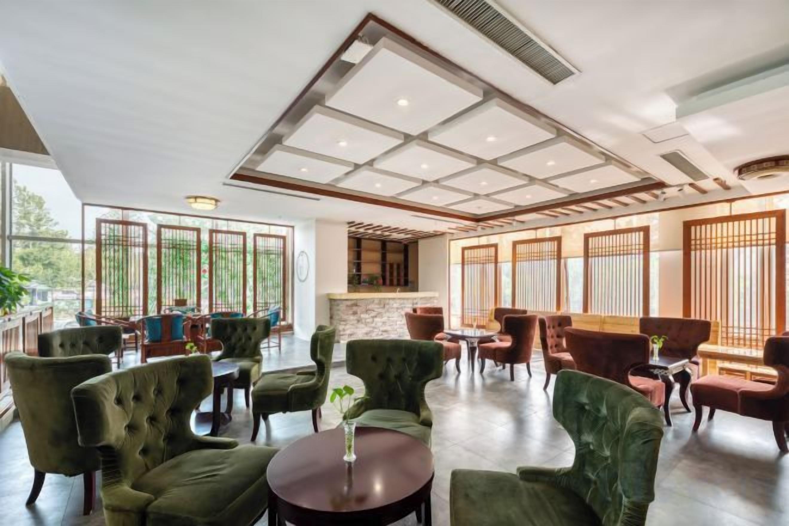 A spacious indoor area with multiple seating arrangements, including round tables and chairs, and large windows allowing natural light.