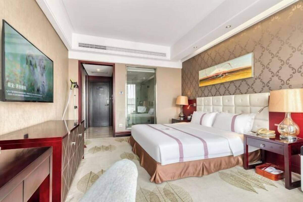 A hotel room with a large bed, a desk, a chair, a TV, and a bathroom visible through an open door.