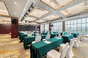 Un salón de conferencias con mesas, sillas, ventanas amplias y un candelabro.
