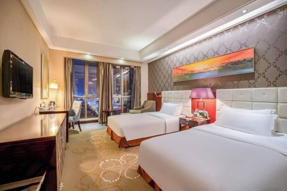 A hotel room with two beds, a desk, a TV, and a city view.