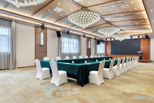 Un salón de conferencias con una mesa larga, sillas blancas y una pantalla de proyector.
