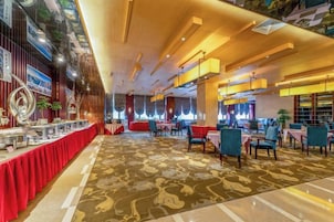 Un vestíbulo de hotel con alfombra roja, un mostrador de recepción y un área de descanso con mesas y sillas.