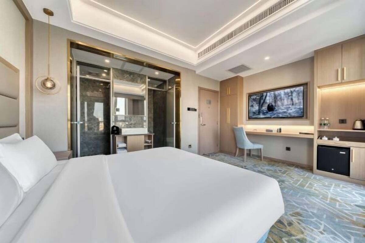 A hotel room with a large bed, a desk with a chair, a television, and a minibar.