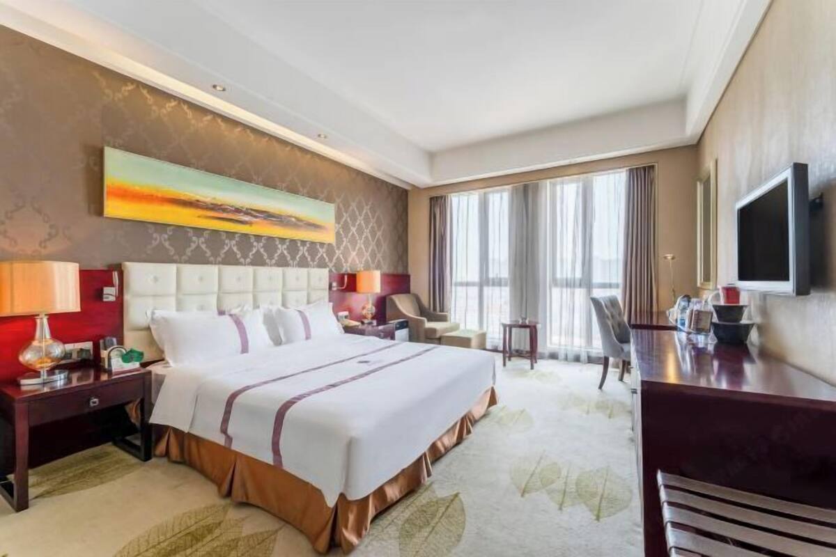 A hotel room with a large bed, a desk, a chair, a TV, and a painting on the wall.
