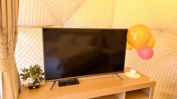 Ein Fernseher auf einem Holzständer mit Fernbedienung, einer kleinen Topfpflanze und Luftballons.