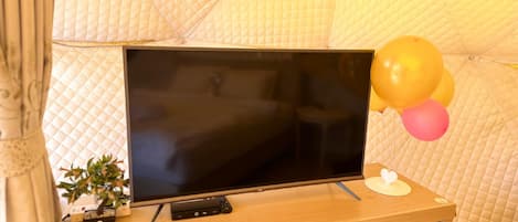 A television on a wooden stand with a remote control, a small potted plant, and balloons.