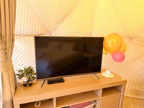 A television on a wooden stand with a remote control, a small potted plant, and balloons.