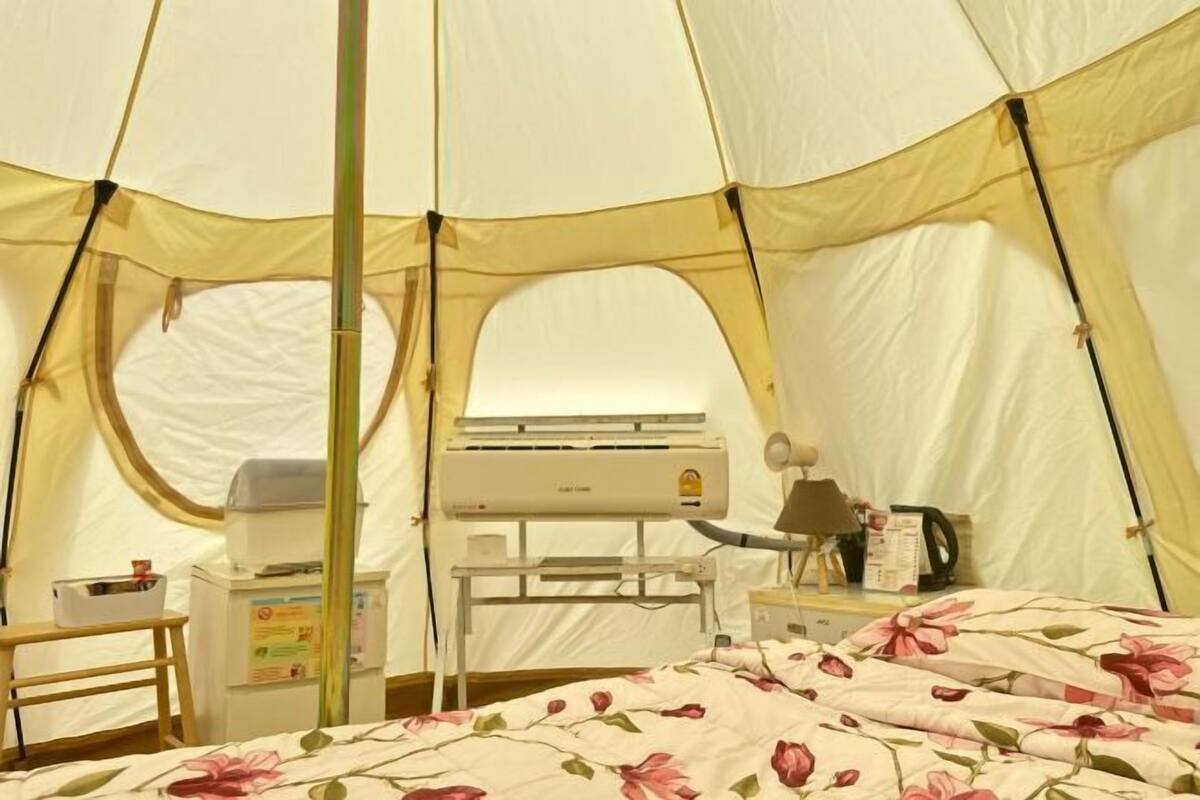 A tent with a bed, a table, a chair, and an air conditioning unit.