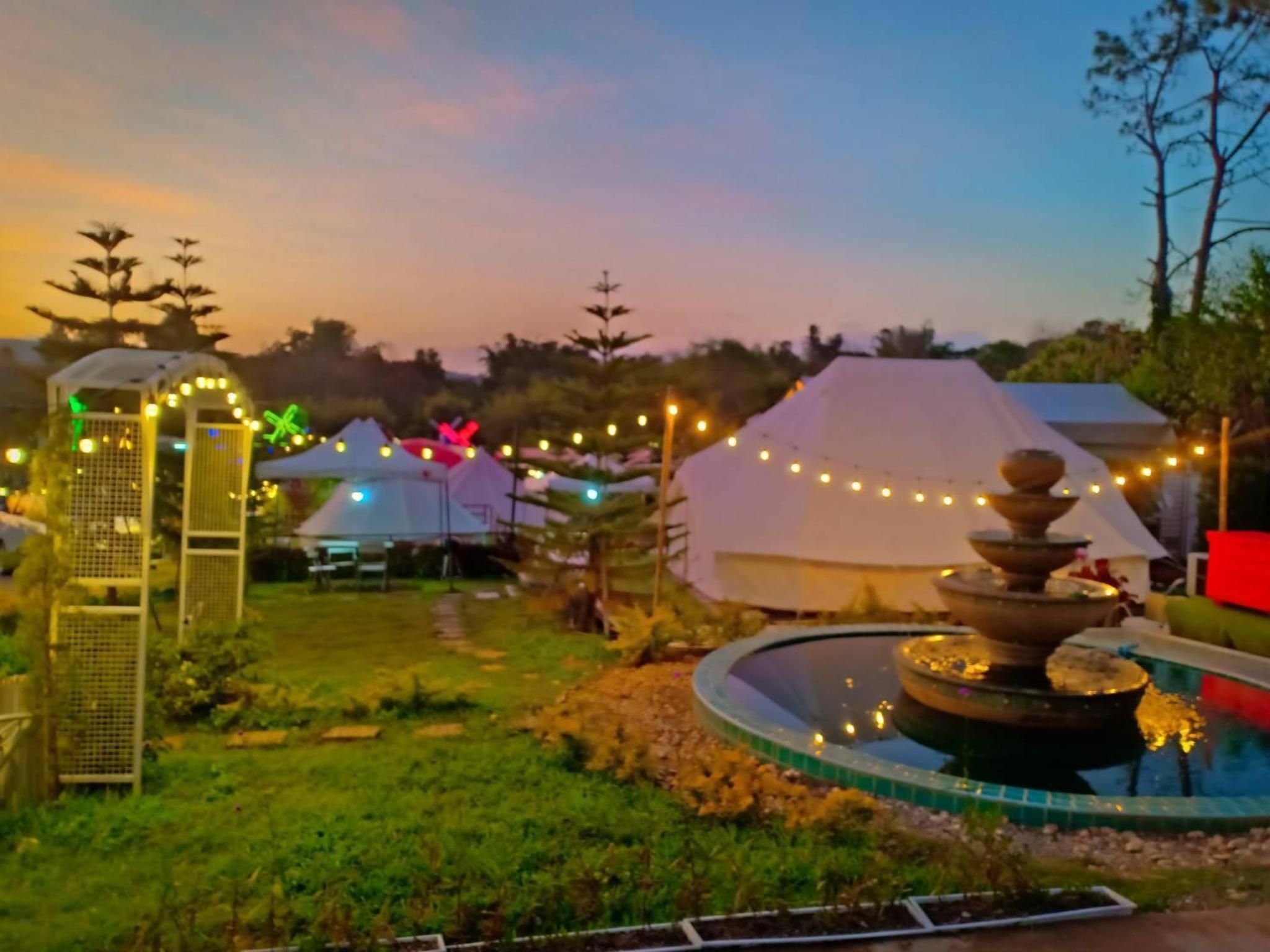 A garden with a fountain, tents, and string lights.