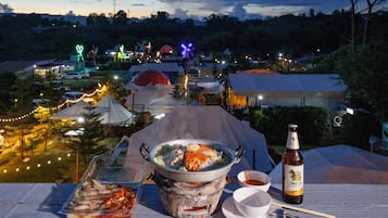A dining table with a pot of soup, a plate of seafood, a beer bottle, and a bowl of sauce.