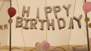Une pièce aménagée avec des tentes, des lits, des ballons formant les mots « JOYEUX ANNIVERSAIRE » et des coussins en forme de cygne.