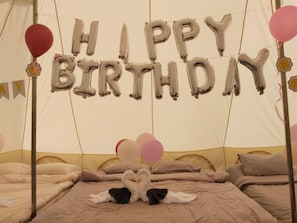 A tented room with beds, balloons spelling 'HAPPY BIRTHDAY,' and swan-shaped pillows.