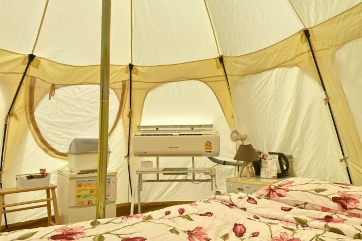 Een tent met een bed, een tafel, een stoel en een airconditioning.