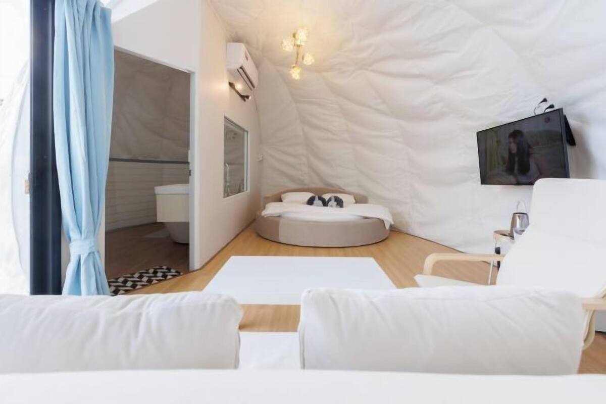 A modern bedroom with a circular bed, a bedside table, a chair, and a wall-mounted TV.