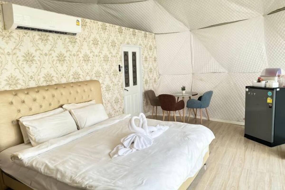A hotel room with a bed, a small table, two chairs, a refrigerator, and an air conditioning unit.