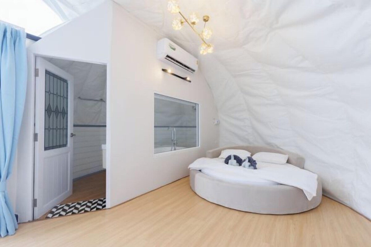 A modern bedroom with a curved bed, a skylight, and a mounted air conditioner.