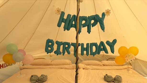 Una carpa decorada con adornos de 'HAPPY BIRTHDAY', dos camas y globos.