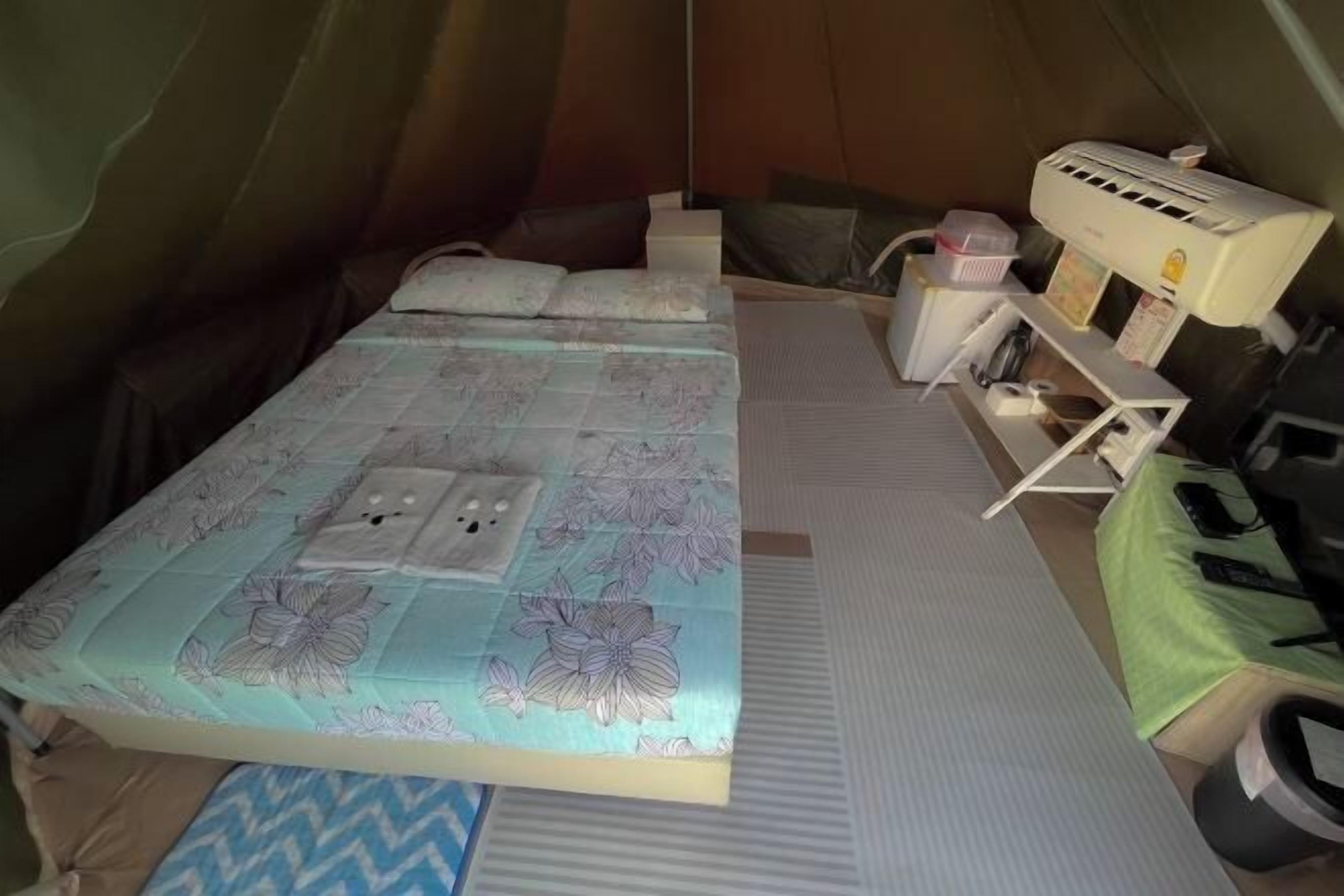 Tenda com cama, mesa pequena, cadeira e ar condicionado.