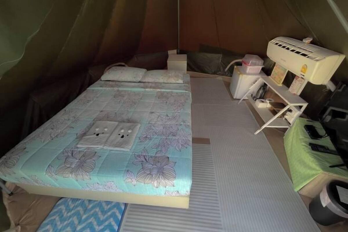 A tent with a bed, a small table, a chair, and an air conditioning unit.