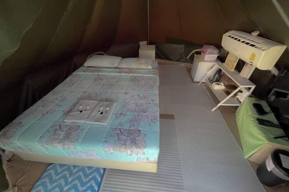 A tent with a bed, a small table, a chair, and an air conditioning unit.