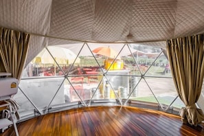 Een kamer met een houten vloer, een groot raam met uitzicht naar buiten en een plafond met een structuur.
