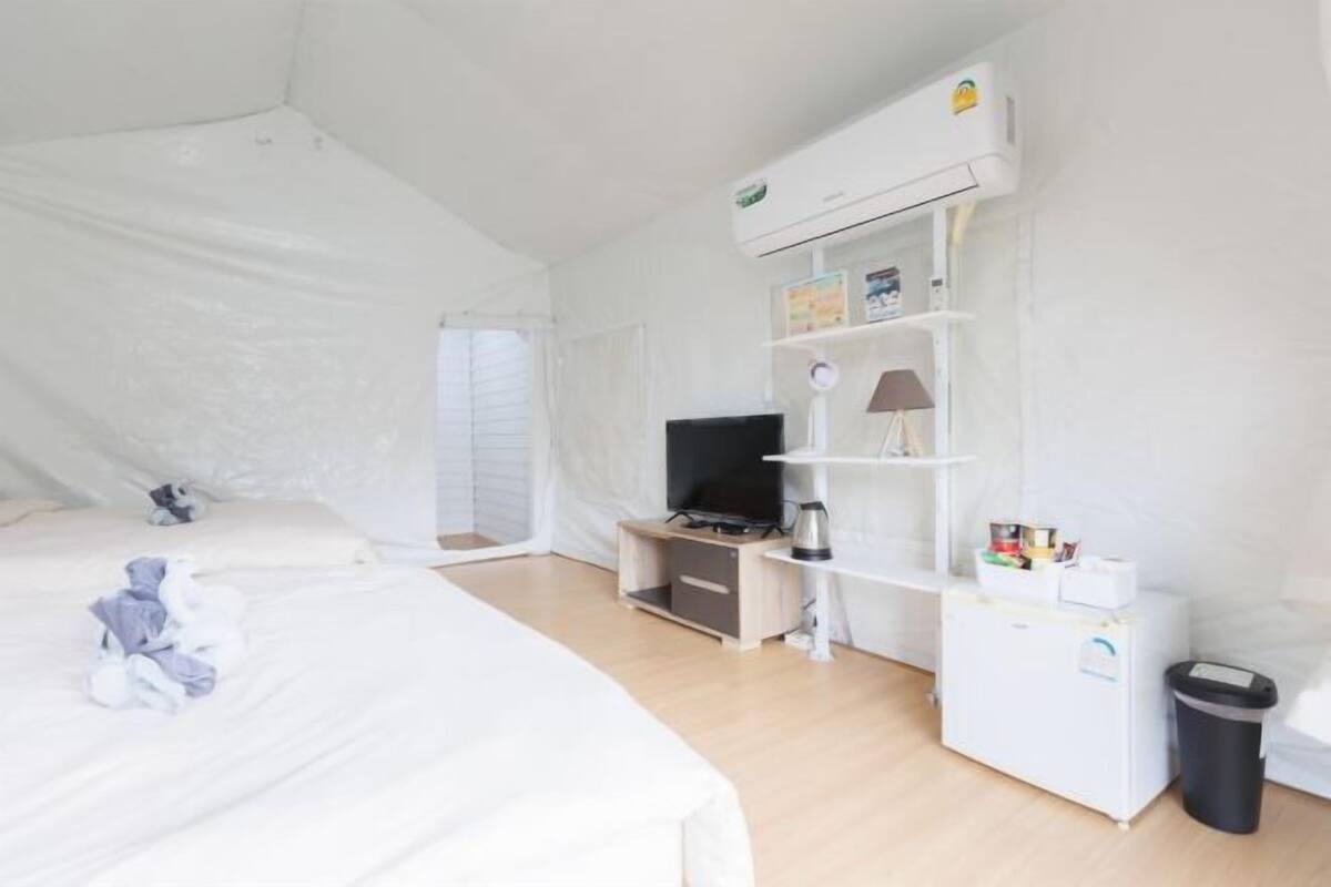 A room with a bed, a TV, a small desk, a lamp, and a refrigerator.