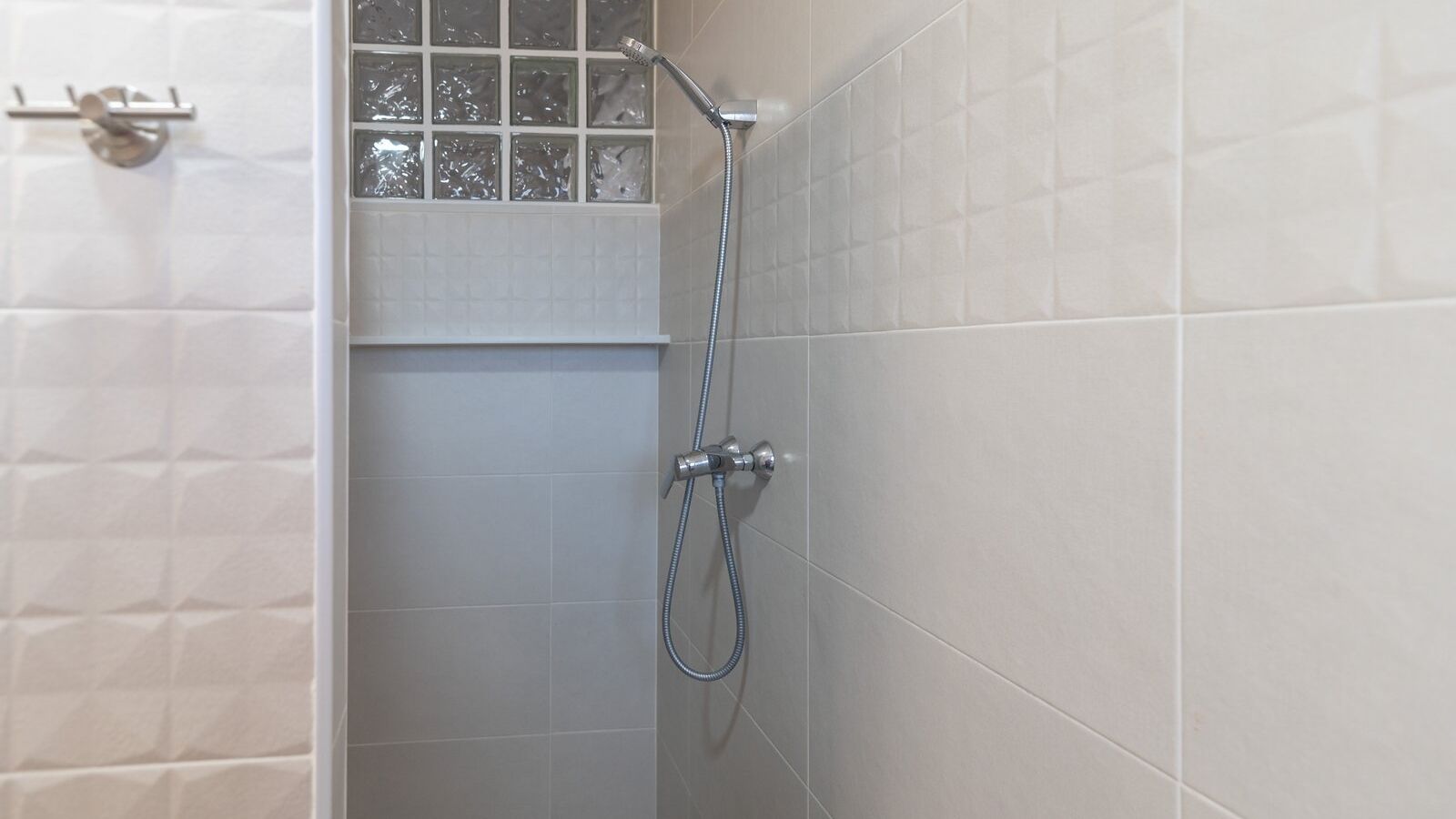 A shower area with a handheld showerhead and a wall-mounted faucet.