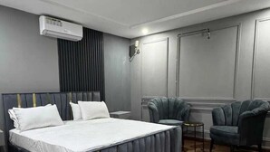 A modern bedroom with a large bed, a grey upholstered armchair, a small table, and a grey rug. - frnish flat  (Islamabad)