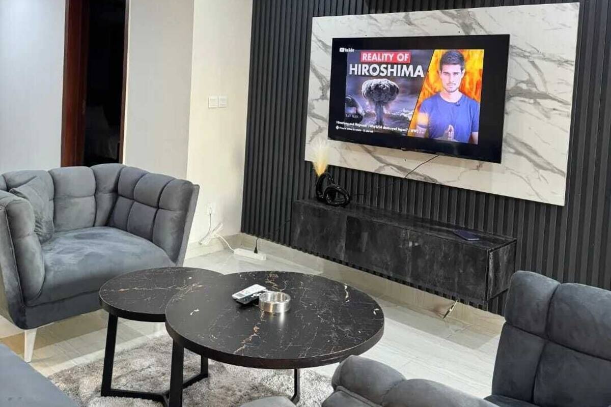 Moderni olohuone, jossa on seinälle asennettu litteänäyttöinen televisio marmoriseinässä, harmaalla kankaalla verhoillut sohvat, musta sohvapöytä ja musta sivupöytä.