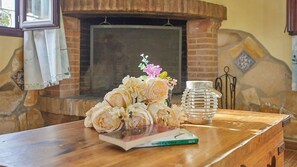A wooden table with a bouquet of flowers, a book, and a lantern in a room with a brick fireplace. - Casa Los Olivos Prado del Rey by Ruralidays (Cádiz)
