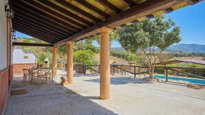 Une terrasse couverte avec une table et des chaises, une piscine et une vue sur les collines.
