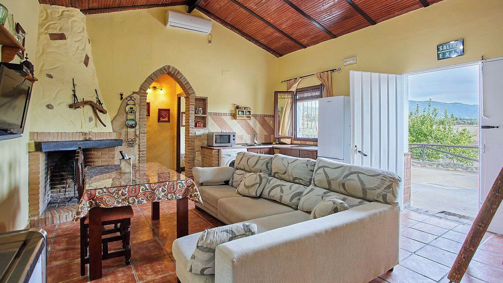 A cozy living room with a fireplace, a sofa, a dining table, and a view of the outdoors.