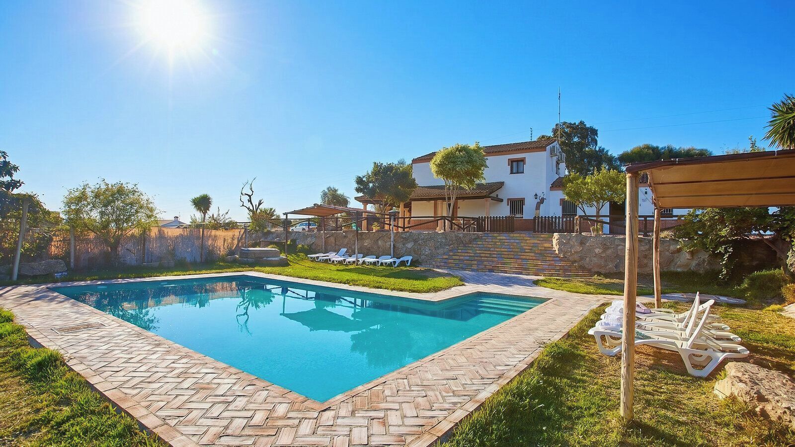 Una piscina rectangular con un borde de baldosas tipo espiga, rodeada de césped y un sendero pavimentado.