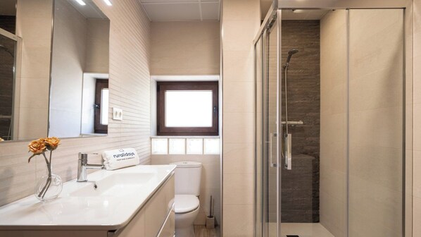 A modern bathroom with a glass shower enclosure, a white sink with a vase of flowers, and a toilet.