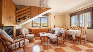 A cozy living room with a fireplace, wooden furniture, a dining area, and a staircase leading to an upper level. - Villa Cuesta Colorada Huétor Santillán by Ruralidays (Granada)
