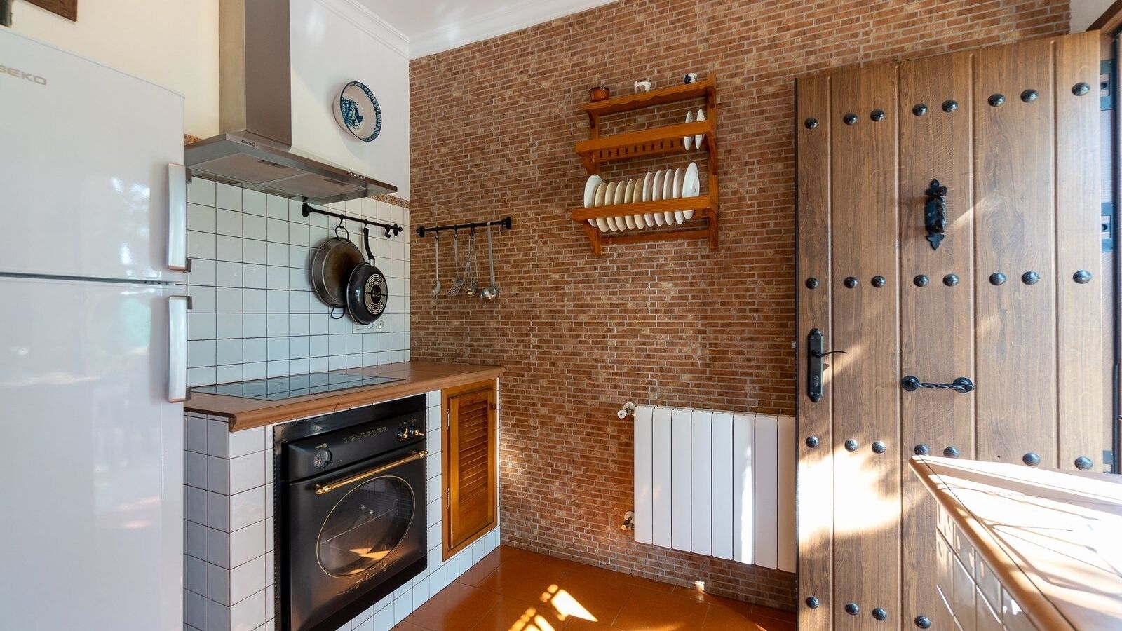A kitchen with a brick wall, a wooden door, and a white refrigerator.