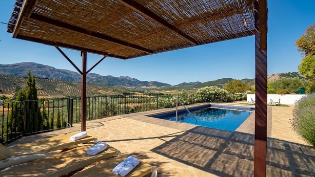 A pool area with a view of mountains, a pergola, and lounge chairs. - La Colina Villanueva del Rosario by Ruralidays (Málaga)