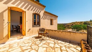 A stone-floored patio with a chair and table, a door leading inside, and a view of the countryside.