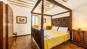 A four-poster bed with a wooden headboard, a stone-tiled floor, and a wooden nightstand with a lamp.
