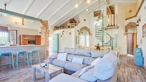 A spacious living area with a large sofa, a kitchen with a bar area, and a spiral staircase. - El Rincón de Marco y María Prado del Rey by Ruralidays (Cádiz)