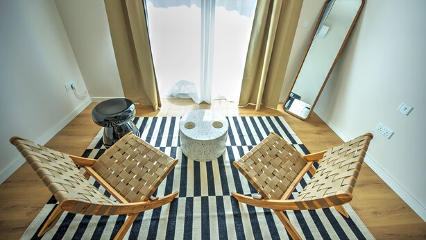Una habitación con dos sillas de madera, una mesa redonda, un espejo y vistas a una noria a través de una ventana con cortinas.