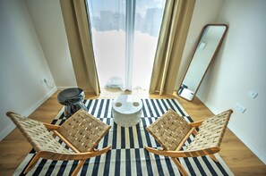 Una habitación con dos sillas de madera, una mesa redonda, un espejo y vistas a una noria a través de una ventana con cortinas.