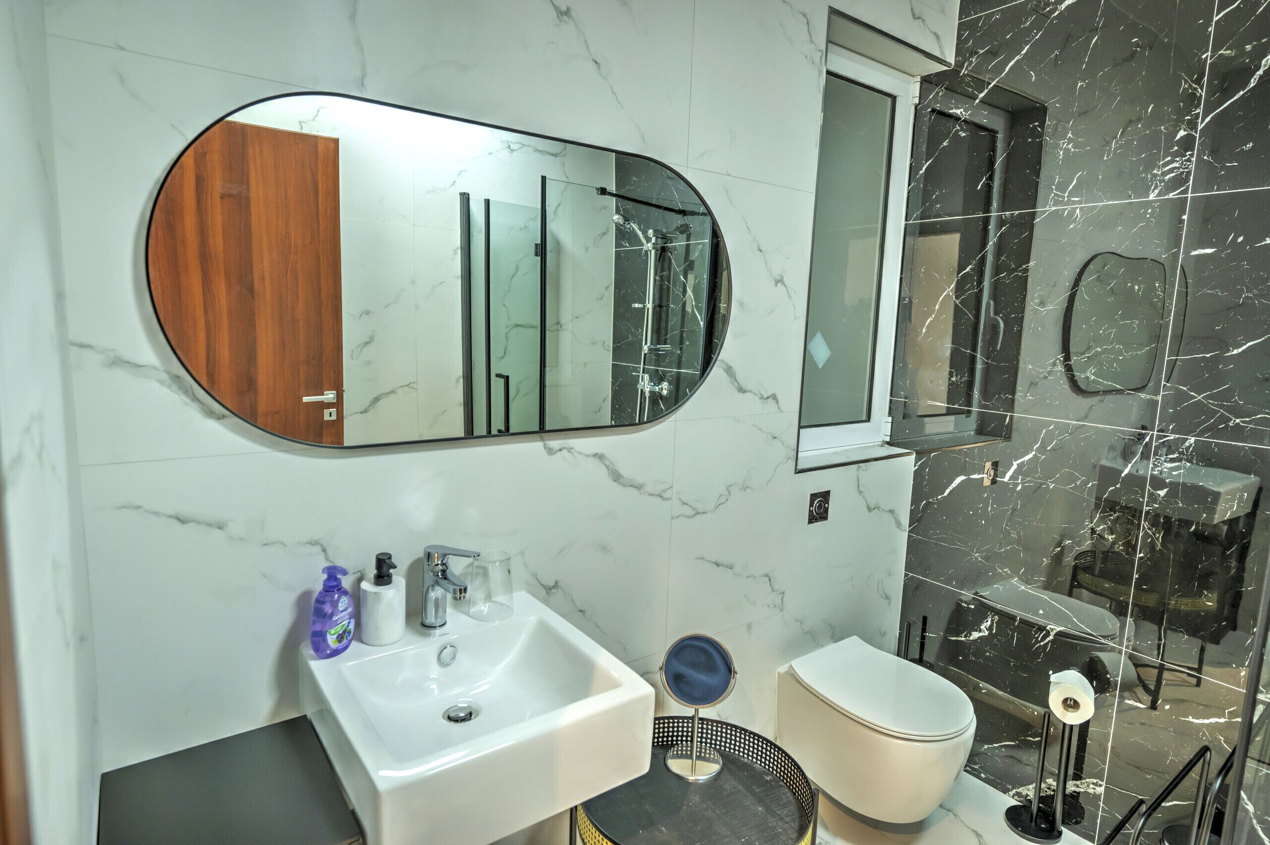 Een moderne badkamer met een marmeren wand, een grote spiegel, een wastafel, toilet en een douchegedeelte.